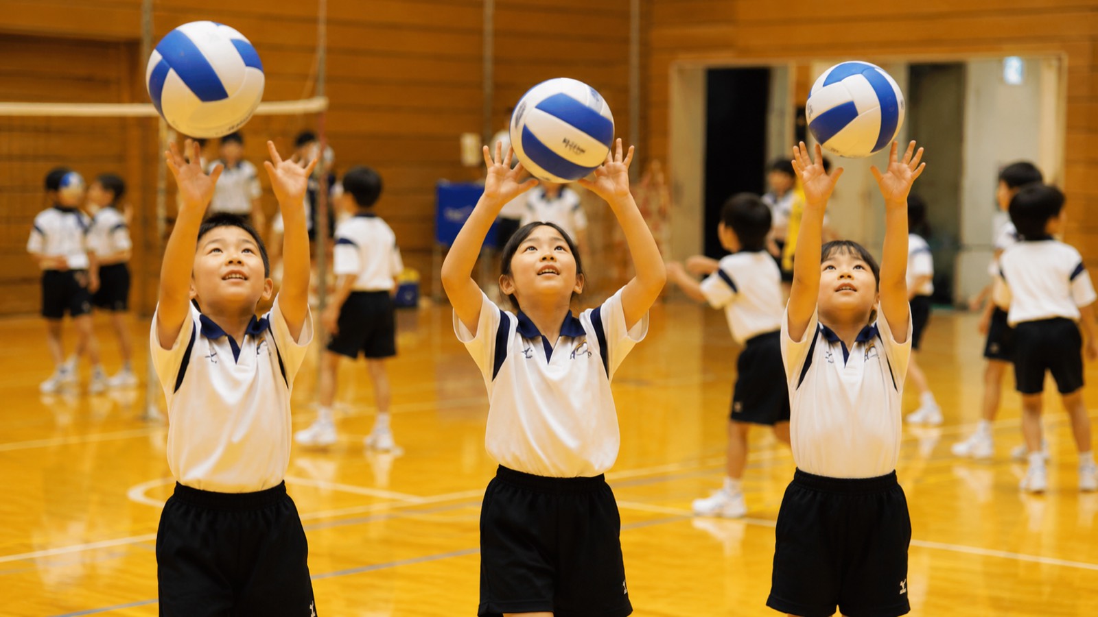 体育館でバレーボールを高く上げて練習する子どもたち（イメージ）