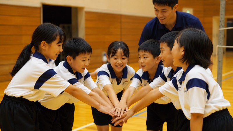 円陣を組んで手を重ねる子どもたち（イメージ）